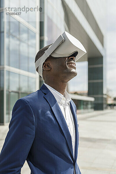 Lächelnder Geschäftsmann trägt an einem sonnigen Tag einen Virtual-Reality-Simulator