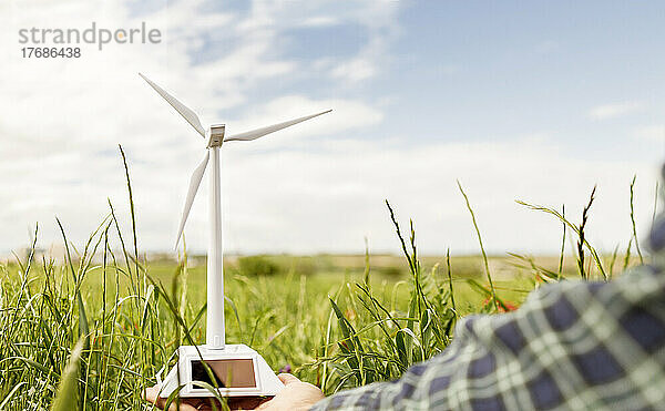 Hand eines Mannes  der ein Windturbinenmodell im grünen Feld hält