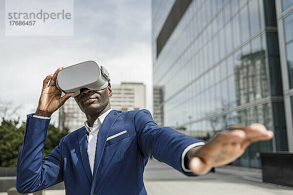 Geschäftsmann mit Virtual-Reality-Simulator gestikuliert vor modernem Bürogebäude