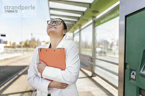 Happy businesswoman holding file folder standing at tram station