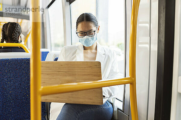 Geschäftsfrau trägt Schutzmaske und benutzt Laptop in der Straßenbahn