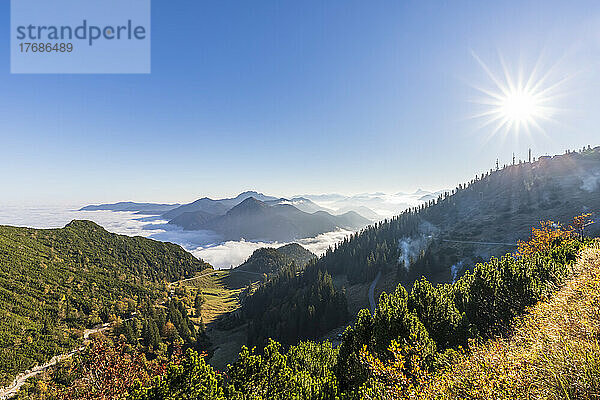 Deutschland  Bayern  Sommersonne scheint über einem bewaldeten Tal in den Bayerischen Voralpen mit dichtem Nebel im Hintergrund