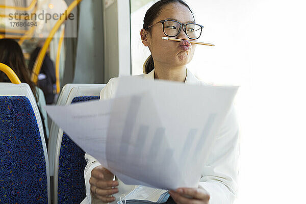 Geschäftsfrau mit Bleistift auf gespitzten Lippen sitzt mit Dokumenten in der Straßenbahn