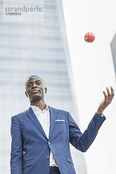 Selbstbewusster junger Geschäftsmann fängt Apfel vor modernem Bürogebäude