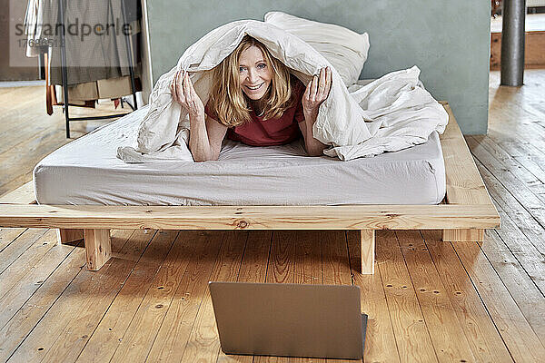 Glückliche Frau  die zu Hause unter einer Decke im Bett liegt