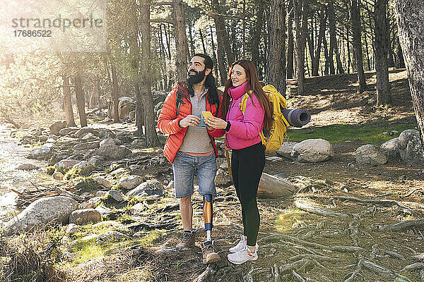 Junge Frau mit Smartphone steht neben behindertem Freund im Wald