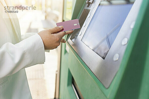 Hand einer Geschäftsfrau  die an der Straßenbahnhaltestelle ein Ticket für den Kauf einer Kreditkarte hält