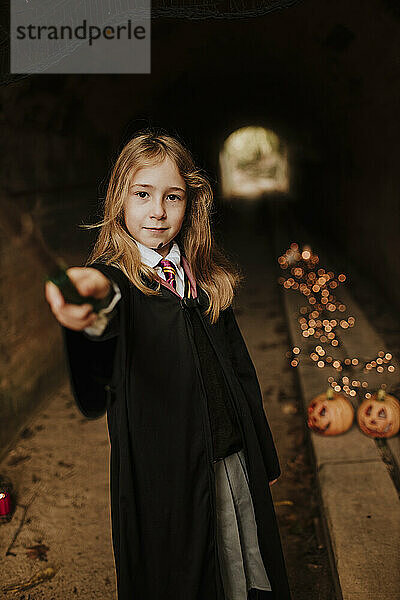 Mädchen mit Zauberstab im Hexenkostüm steht im gruseligen Tunnel