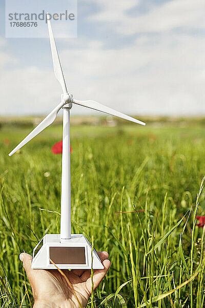 Mann mit Windturbinenmodell im grünen Feld an einem sonnigen Tag