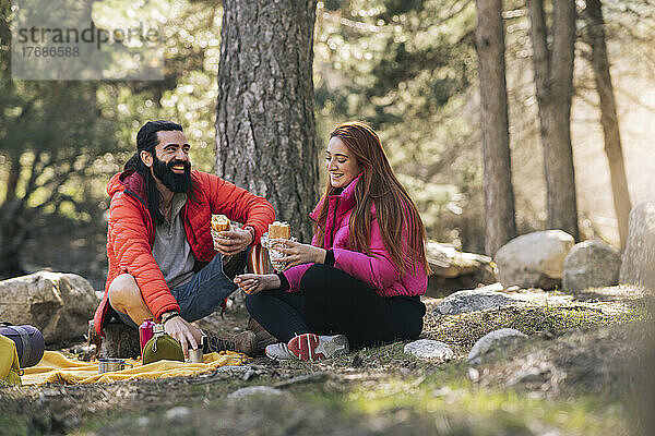 Fröhlicher Mann und Frau mit Essen sitzen im Wald