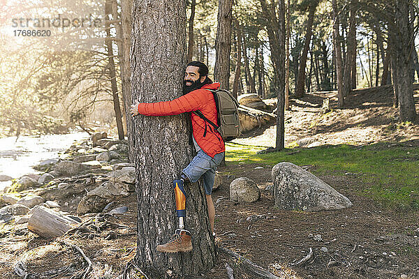 Glücklicher behinderter Mann umarmt Baum im Wald