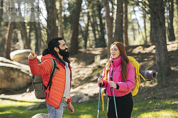 Junge Frau spricht mit ihrem Freund  der einen Rucksack trägt und in den Wald zeigt