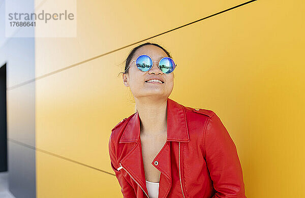 Lächelnde Frau mit Sonnenbrille steht vor gelber Wand