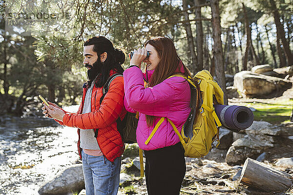 Mann benutzt Smartphone von Freundin und schaut durch ein Fernglas im Wald