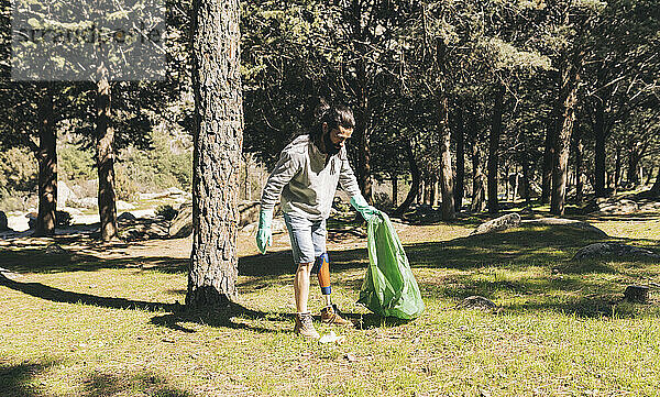 Behinderter Mann mit Müllsack im Wald an sonnigem Tag