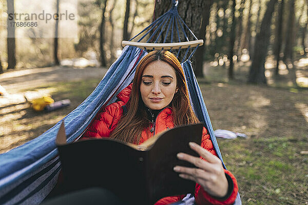 Junge Frau liest Tagebuch und entspannt sich in der Hängematte