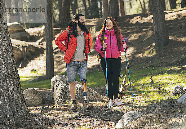 Lächelnder behinderter Mann im Gespräch mit Freundin  die mit Wanderstock im Wald steht