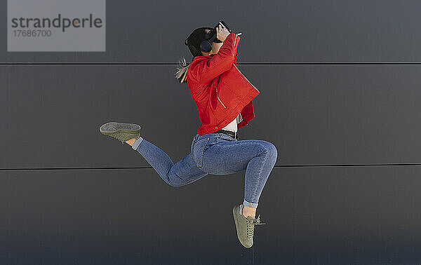 Verspielte Frau mit Virtual-Reality-Simulator springt vor graue Wand