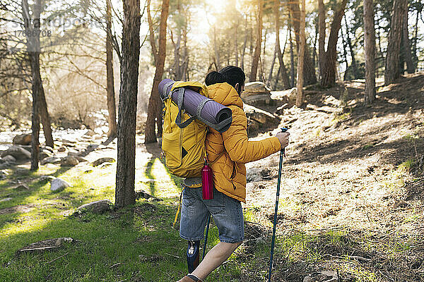 Behinderter Mann mit Rucksack läuft mit Wanderstöcken im Wald