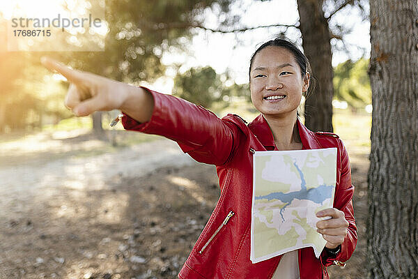 Lächelnde Frau hält Karte in der Hand und gestikuliert im Wald