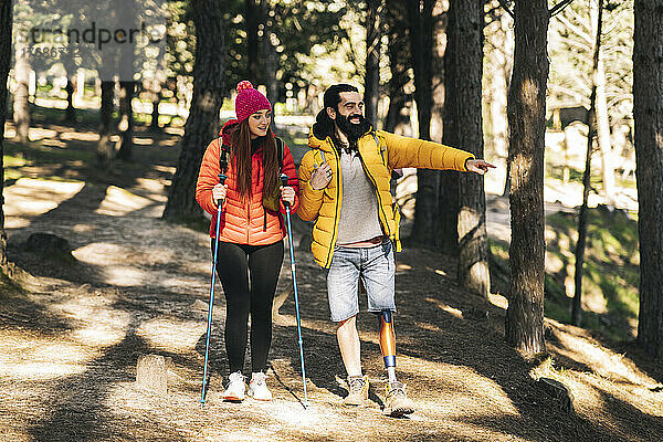 Glücklicher behinderter Mann zeigt weg  während Frau mit Wanderstock im Wald spaziert
