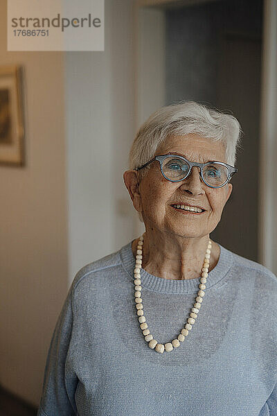 Lächelnde ältere Frau mit Brille steht zu Hause