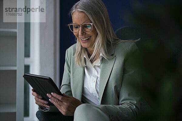Glückliche Geschäftsfrau mit Tablet-PC auf Stuhl sitzend