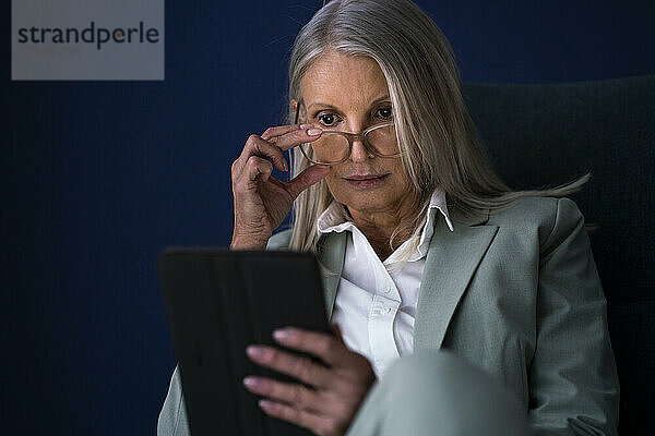 Geschäftsfrau hält eine Brille und schaut sich einen Tablet-PC an