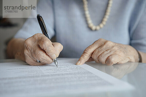 Hands of senior woman writing on paper with pen