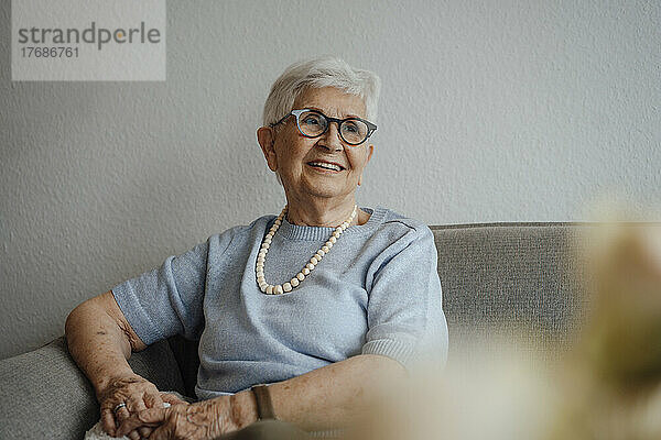 Lächelnde ältere Frau sitzt zu Hause auf dem Sofa