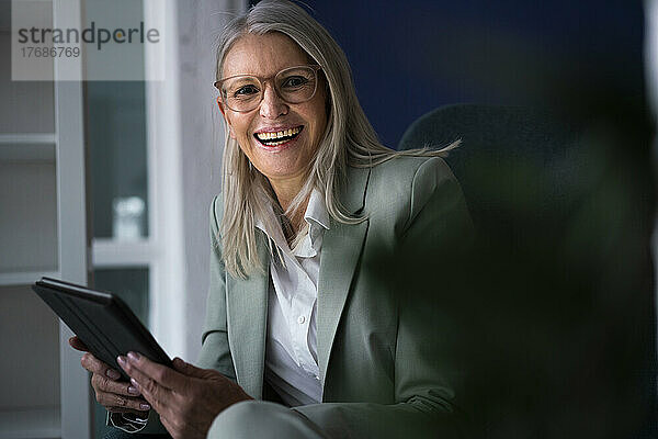 Ältere Geschäftsfrau hält lachend einen Tablet-PC in der Hand