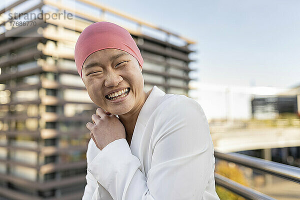 Fröhliche junge Frau mit rosa Kopftuch vor dem Gebäude