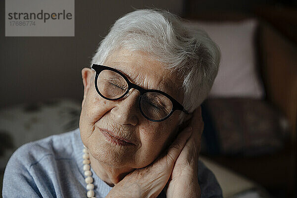 Ältere Frau lehnt zu Hause den Kopf auf die Hände und die Augen sind geschlossen