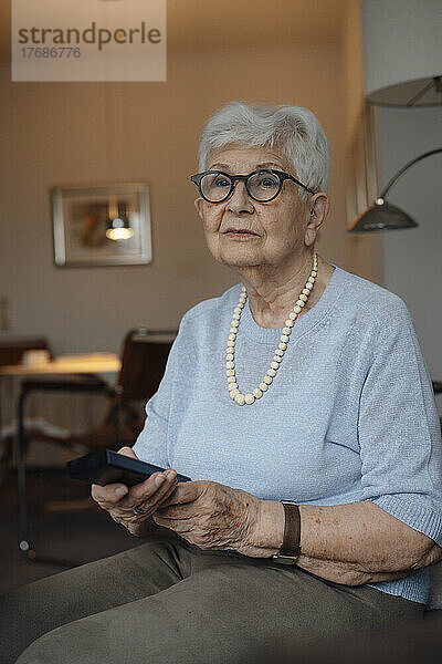 Ältere Frau mit Fernbedienung sitzt zu Hause
