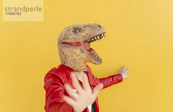 Playful woman wearing dinosaur mask against yellow background