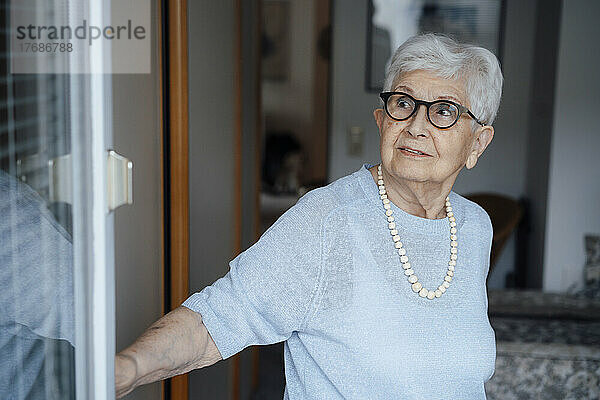 Ältere Frau mit weißen Haaren steht vor der Tür