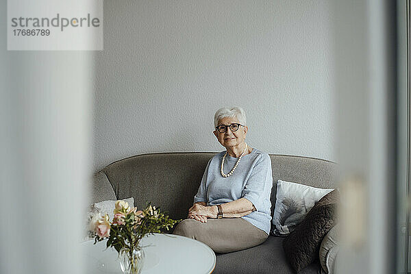 Lächelnde ältere Frau sitzt zu Hause auf dem Sofa im Wohnzimmer