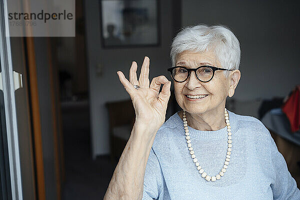 Glückliche ältere Frau mit Brille zeigt eine Geste mit dem OK-Zeichen