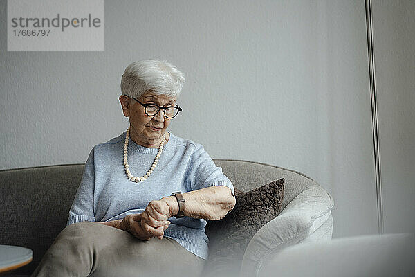 Ältere Frau  die zu Hause sitzt und die Zeit auf der Armbanduhr überprüft