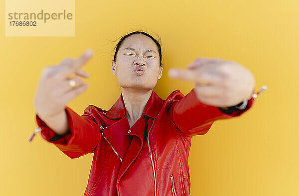 Playful woman showing middle finger against yellow background