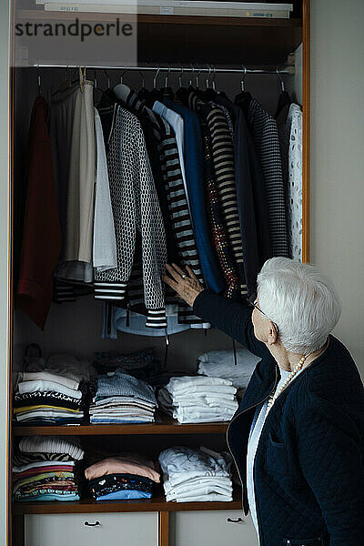 Ältere Frau wählt Kleidung im Schrank zu Hause aus