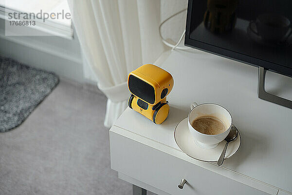 KI-Spielzeugroboter bei Kaffeetasse auf dem Tisch zu Hause