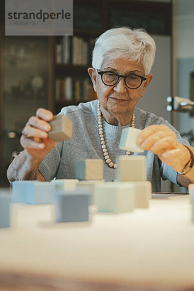 Lächelnde ältere Frau  die zu Hause mit Bauklötzen spielt