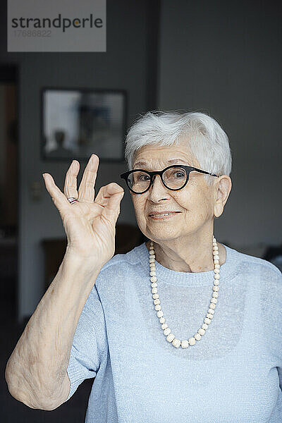 Lächelnde ältere Frau mit Brille zeigt eine OK-Geste