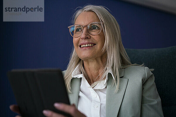 Lächelnde Geschäftsfrau  die darüber nachdenkt  einen Tablet-PC in der Hand zu halten