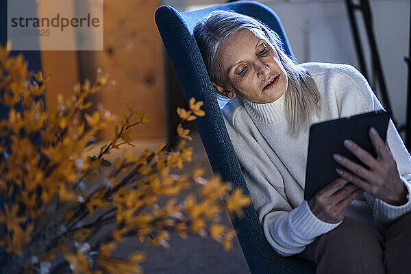 Ältere Frau benutzt einen Tablet-PC  der auf einem Stuhl ruht