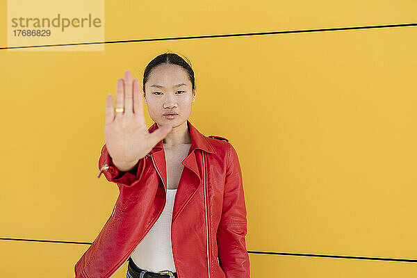 Junge Frau gestikuliert mit der Hand Stoppschild vor gelber Wand
