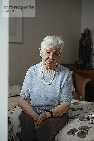 Besorgte ältere Frau sitzt zu Hause im Bett