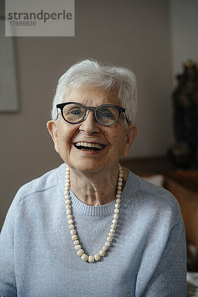 Glückliche ältere Frau mit Brille sitzt zu Hause