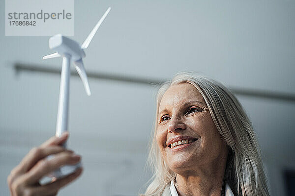 Lächelnde Geschäftsfrau blickt im Büro auf das Modell einer Windkraftanlage